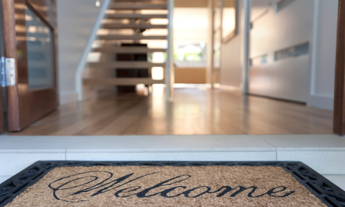 Welcome mat in front of open door of house for sale