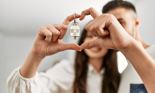 Young couple doing heart symbol with fingers holding key of new home